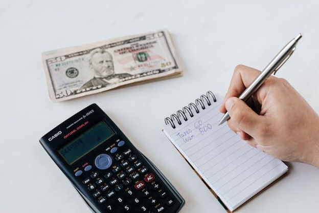 Person writing in a notebook, a calculator, and some money